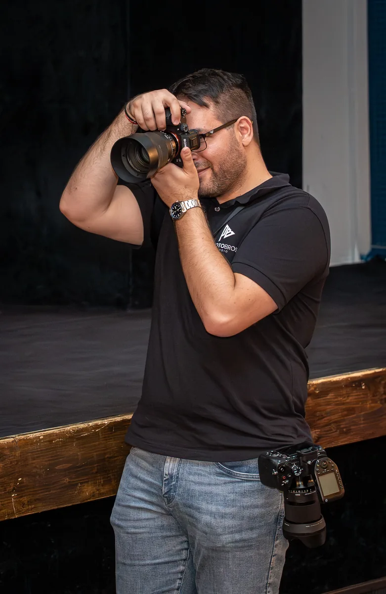 A PhotoBros photographer shooting with a long lens, a second camera on his hip