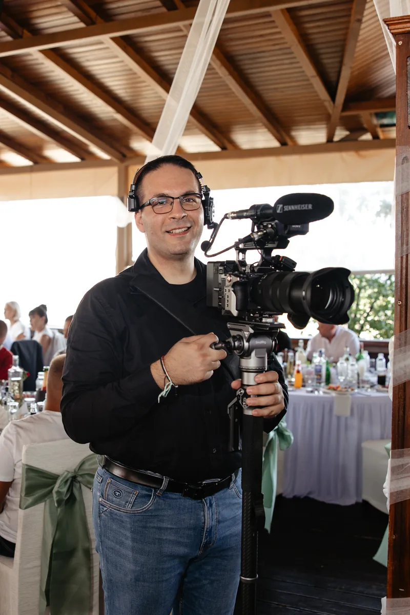 Ilko filming a wedding reception with a camera on a monopod, headphones on